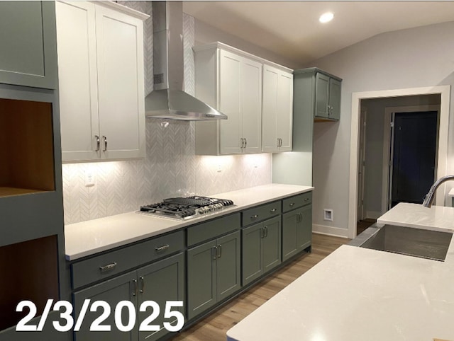 kitchen with wall chimney exhaust hood, sink, stainless steel gas cooktop, vaulted ceiling, and white cabinets