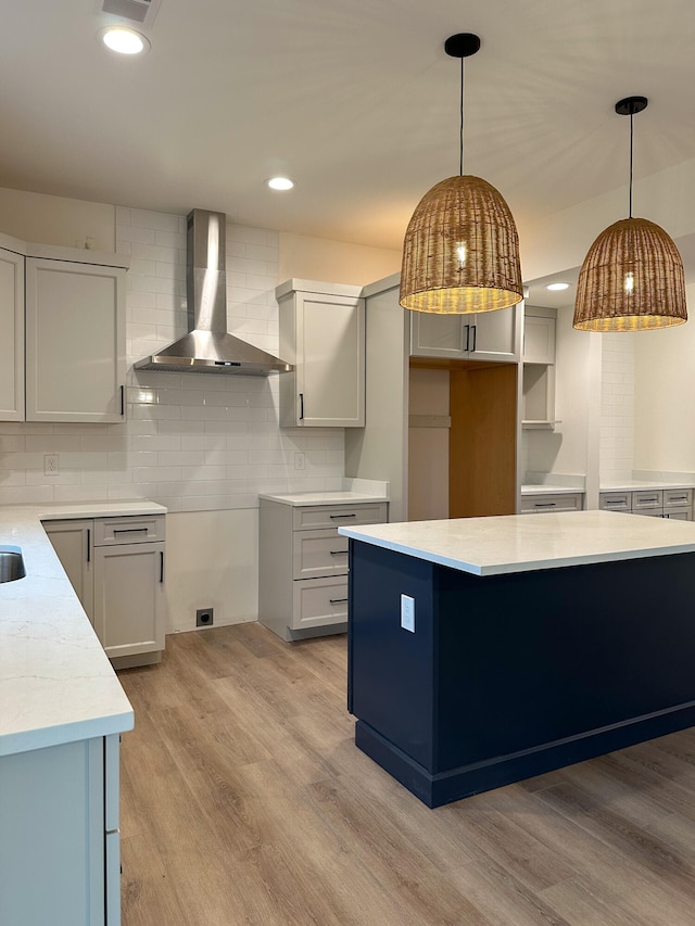 kitchen with backsplash, pendant lighting, wall chimney exhaust hood, and light hardwood / wood-style floors