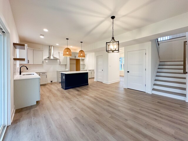 kitchen with light hardwood / wood-style floors, white cabinetry, a kitchen island, wall chimney range hood, and pendant lighting