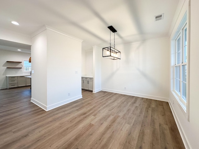 unfurnished dining area with ornamental molding, wood-type flooring, a healthy amount of sunlight, and an inviting chandelier