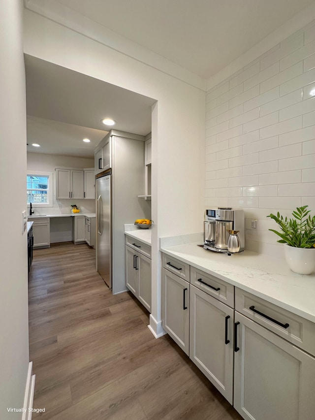 kitchen featuring wood-type flooring, crown molding, backsplash, stainless steel refrigerator, and light stone countertops