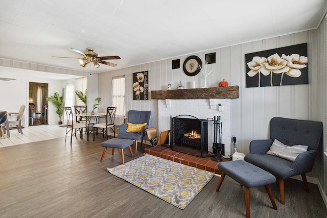 living area with ceiling fan, a fireplace, and dark wood-type flooring