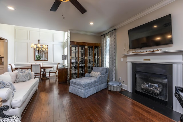 living room with dark wood-type flooring, ceiling fan with notable chandelier, and ornamental molding