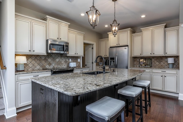 kitchen with pendant lighting, a kitchen island with sink, dark wood-type flooring, tasteful backsplash, and stainless steel appliances