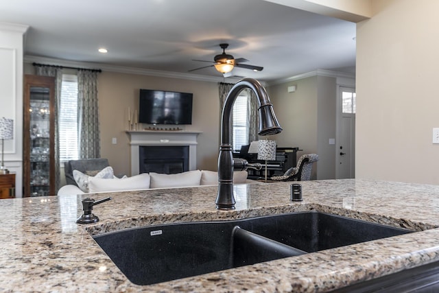 kitchen with light stone counters, ceiling fan, crown molding, and sink