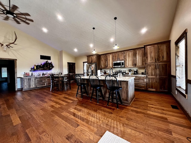 kitchen with a kitchen bar, dark hardwood / wood-style flooring, stainless steel appliances, hanging light fixtures, and a large island