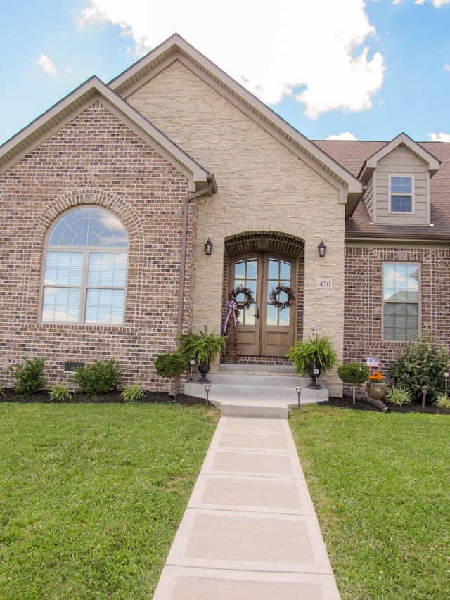 view of exterior entry featuring a lawn, stone siding, french doors, and brick siding