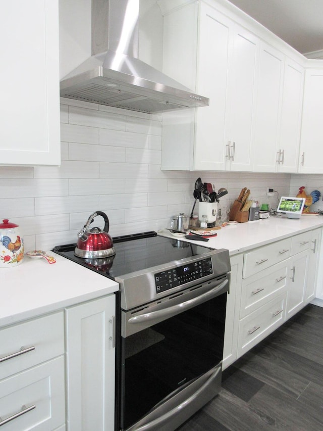 kitchen with wall chimney exhaust hood, white cabinetry, stainless steel electric stove, backsplash, and light countertops