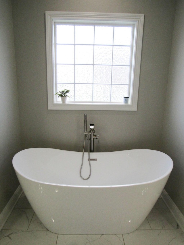 full bathroom with baseboards, marble finish floor, a freestanding tub, and a wealth of natural light