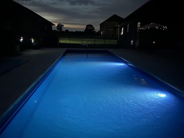 pool at night with a patio, a fenced in pool, and fence