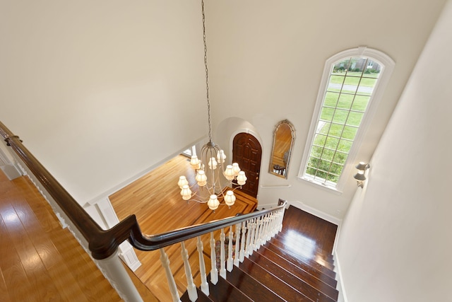 staircase with hardwood / wood-style flooring, plenty of natural light, and a notable chandelier