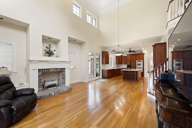 living room featuring a towering ceiling, light wood-type flooring, ceiling fan, crown molding, and a fireplace