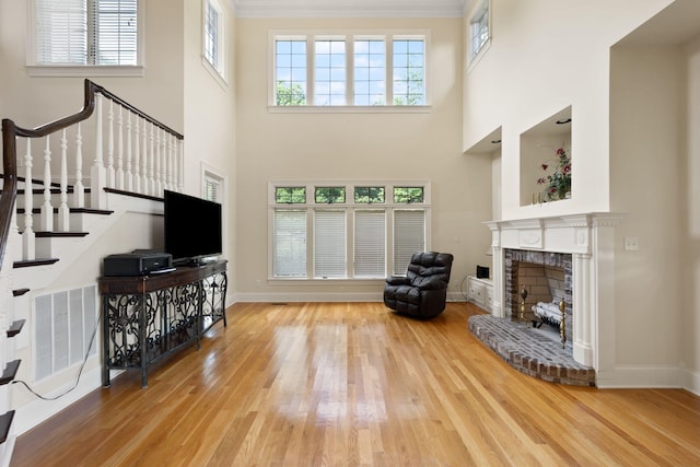 living room with light wood-type flooring, a towering ceiling, and a brick fireplace