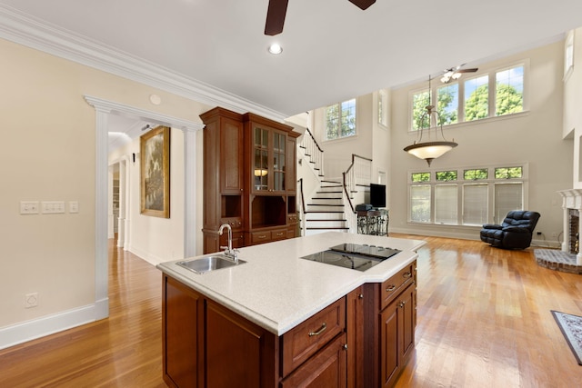 kitchen featuring black electric stovetop, a brick fireplace, ornamental molding, sink, and light hardwood / wood-style flooring