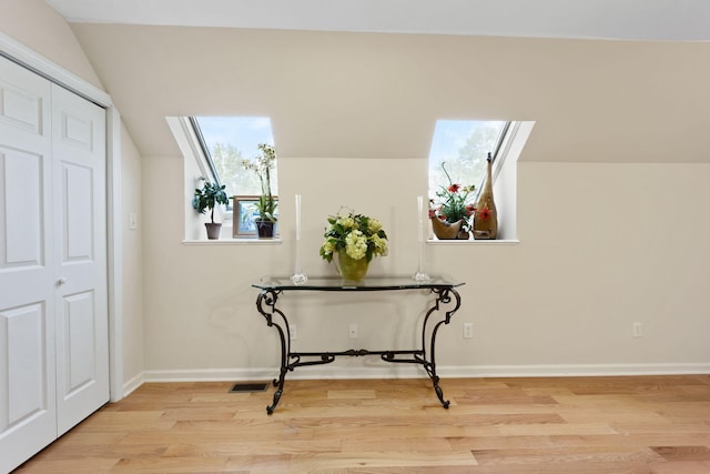 hallway featuring light wood-type flooring and lofted ceiling with skylight