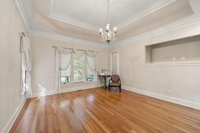 unfurnished room featuring hardwood / wood-style floors, a notable chandelier, a raised ceiling, and crown molding