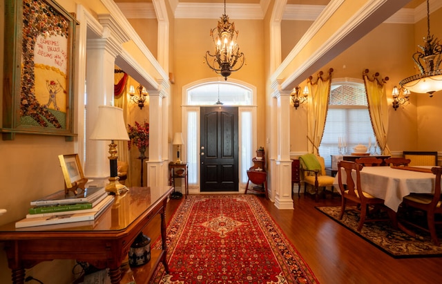 entryway with crown molding, ornate columns, wood-type flooring, a notable chandelier, and a high ceiling