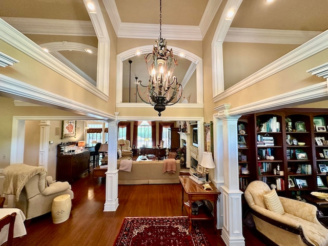 interior space featuring crown molding, ornate columns, an inviting chandelier, a high ceiling, and hardwood / wood-style flooring