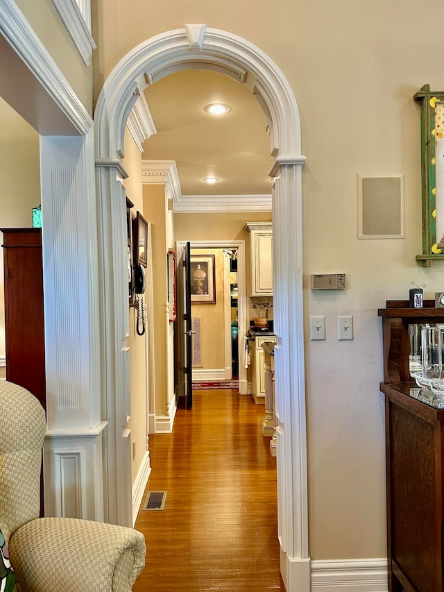 hallway with decorative columns, ornamental molding, and wood-type flooring