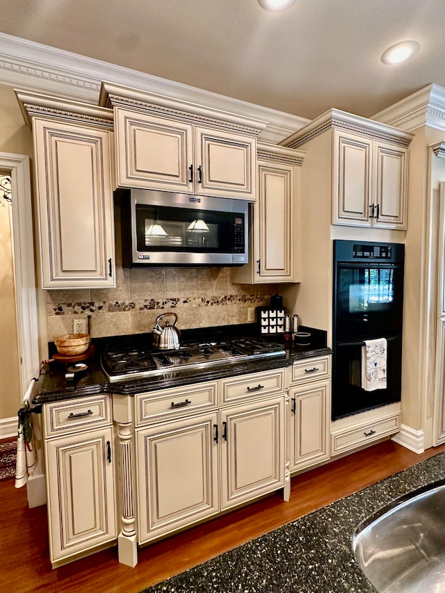 kitchen featuring crown molding, dark wood-type flooring, cream cabinetry, appliances with stainless steel finishes, and tasteful backsplash