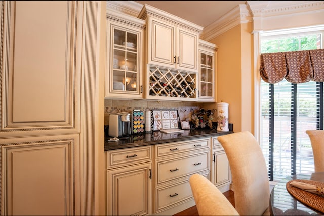 bar with crown molding, backsplash, dark stone countertops, and cream cabinetry