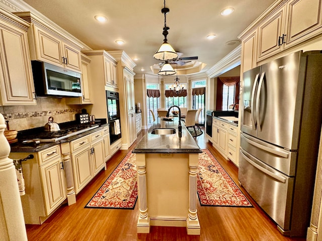 kitchen with ornamental molding, appliances with stainless steel finishes, a kitchen island with sink, hardwood / wood-style flooring, and decorative light fixtures