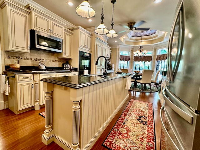 kitchen featuring ornamental molding, a center island with sink, cream cabinetry, appliances with stainless steel finishes, and wood-type flooring