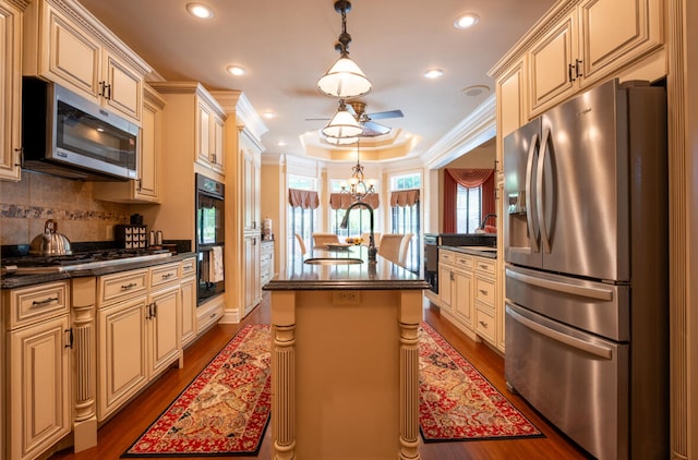 kitchen with an island with sink, dark wood-type flooring, ceiling fan with notable chandelier, backsplash, and appliances with stainless steel finishes