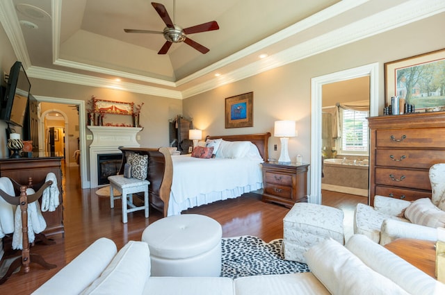 bedroom featuring dark hardwood / wood-style floors, ceiling fan, crown molding, a raised ceiling, and connected bathroom