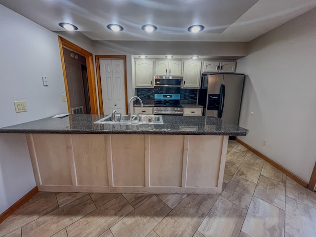 kitchen with backsplash, stainless steel appliances, sink, kitchen peninsula, and dark stone counters