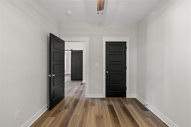 empty room featuring a barn door, ceiling fan, and dark hardwood / wood-style flooring