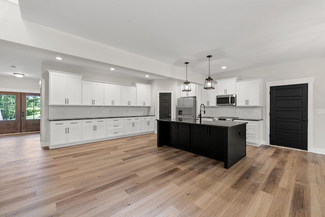 kitchen with backsplash, a kitchen island with sink, hanging light fixtures, white cabinetry, and stainless steel appliances