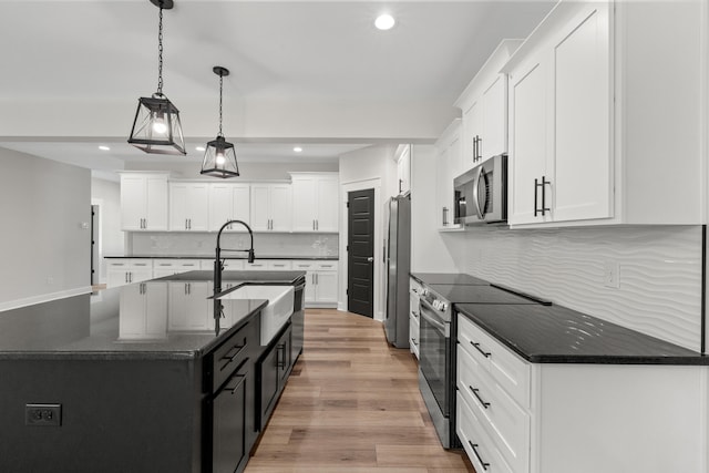 kitchen featuring appliances with stainless steel finishes, tasteful backsplash, pendant lighting, white cabinetry, and an island with sink