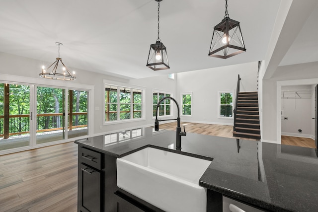 kitchen with sink, hanging light fixtures, dark stone countertops, light wood-type flooring, and a notable chandelier