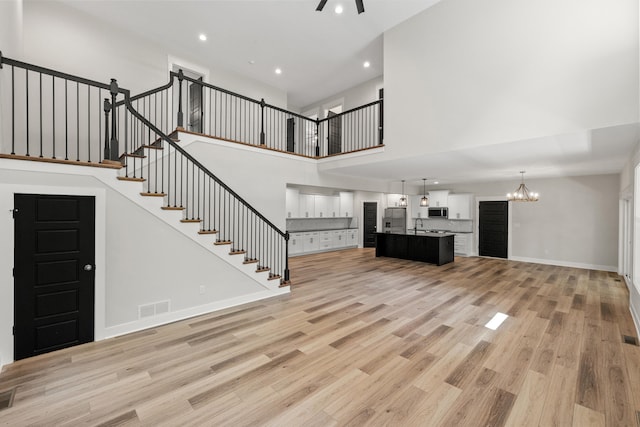 unfurnished living room featuring ceiling fan with notable chandelier, a high ceiling, and light wood-type flooring