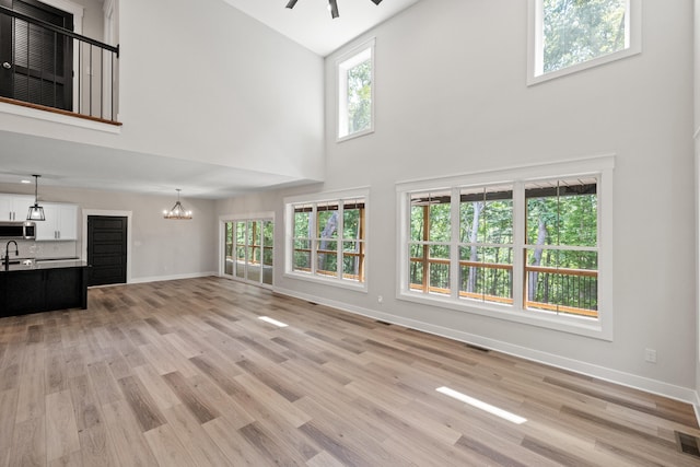 unfurnished living room with a high ceiling, ceiling fan with notable chandelier, light hardwood / wood-style flooring, and sink