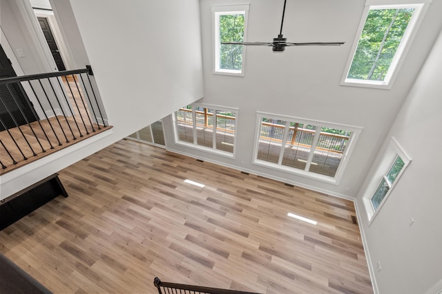 unfurnished living room featuring ceiling fan, a towering ceiling, and light hardwood / wood-style floors