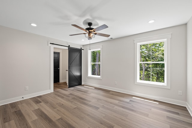 unfurnished bedroom with a barn door, light hardwood / wood-style floors, and ceiling fan