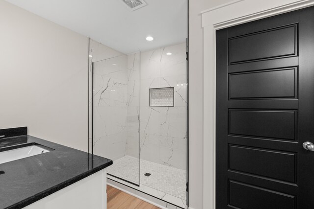 bathroom with wood-type flooring, vanity, and a tile shower