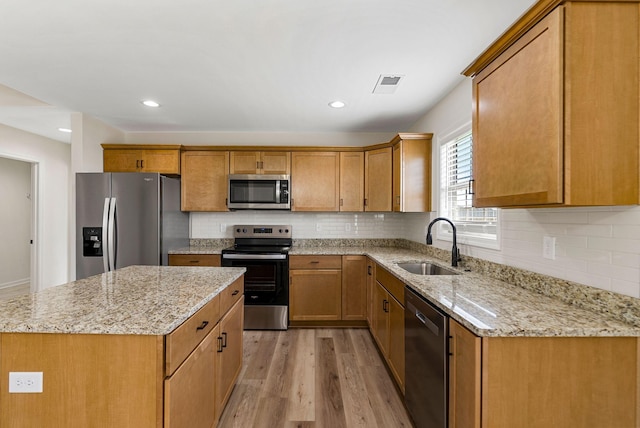 kitchen featuring light wood-type flooring, brown cabinetry, stainless steel appliances, and a sink