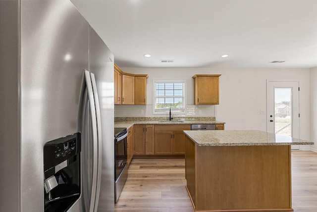 kitchen featuring appliances with stainless steel finishes, a sink, light wood-style flooring, and a center island