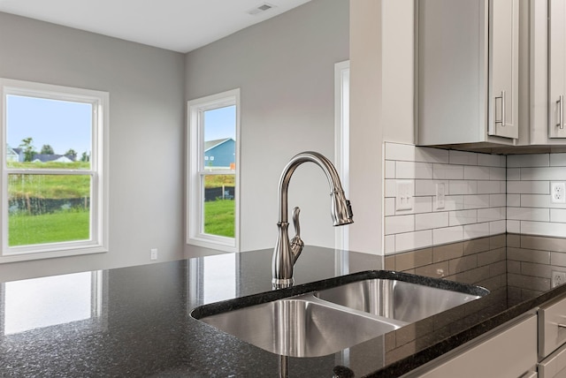 kitchen with tasteful backsplash, dark stone counters, sink, white cabinetry, and plenty of natural light