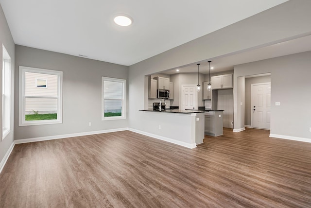 unfurnished living room featuring a healthy amount of sunlight, sink, and dark wood-type flooring