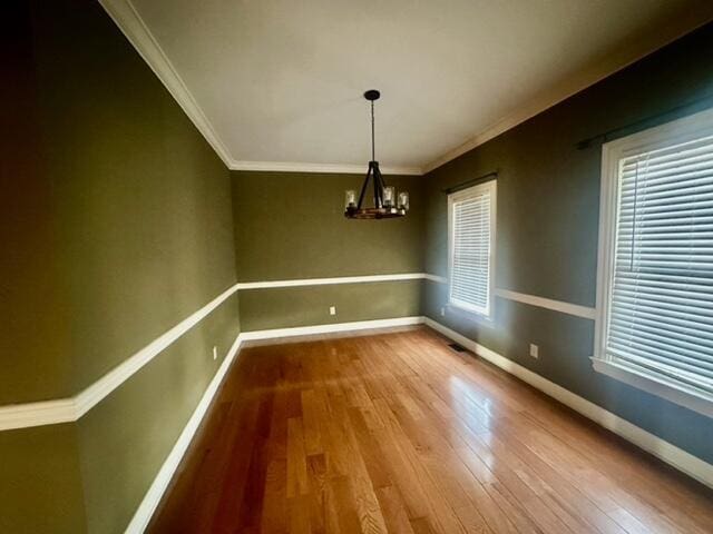 unfurnished dining area with crown molding, an inviting chandelier, and hardwood / wood-style flooring