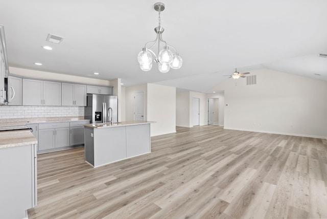 kitchen featuring ceiling fan with notable chandelier, a kitchen island with sink, stainless steel refrigerator with ice dispenser, light wood-type flooring, and tasteful backsplash