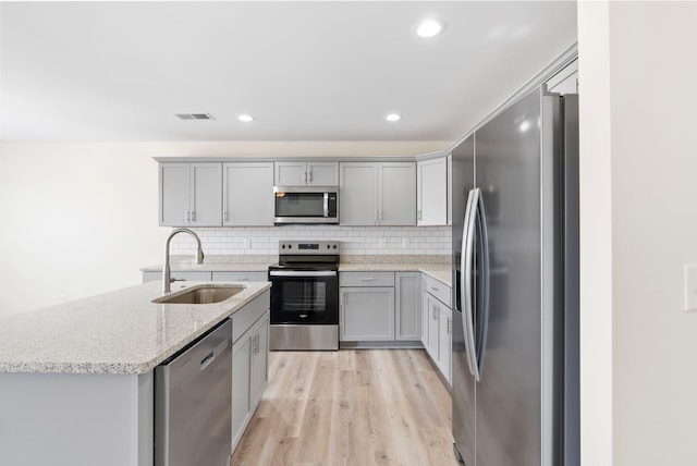 kitchen with appliances with stainless steel finishes, light wood-type flooring, sink, tasteful backsplash, and light stone counters