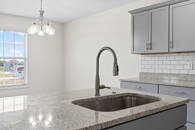 kitchen featuring backsplash, light stone counters, a chandelier, sink, and decorative light fixtures