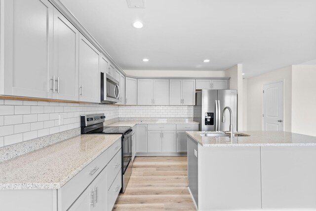 kitchen featuring decorative backsplash, light stone countertops, stainless steel appliances, and light hardwood / wood-style floors