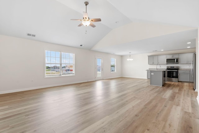 unfurnished living room featuring high vaulted ceiling, sink, light wood-type flooring, and ceiling fan with notable chandelier