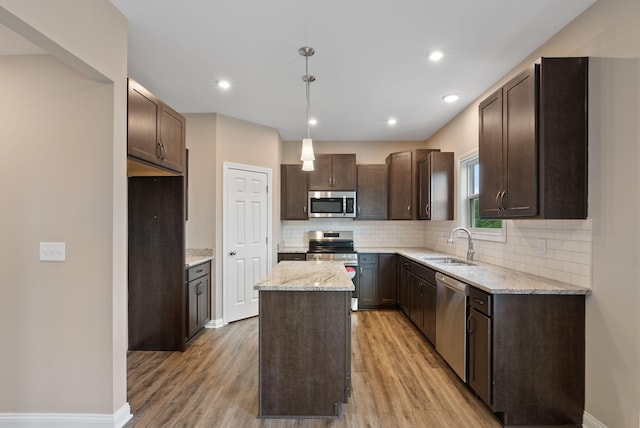 kitchen with stainless steel appliances, sink, decorative light fixtures, light wood-type flooring, and a kitchen island